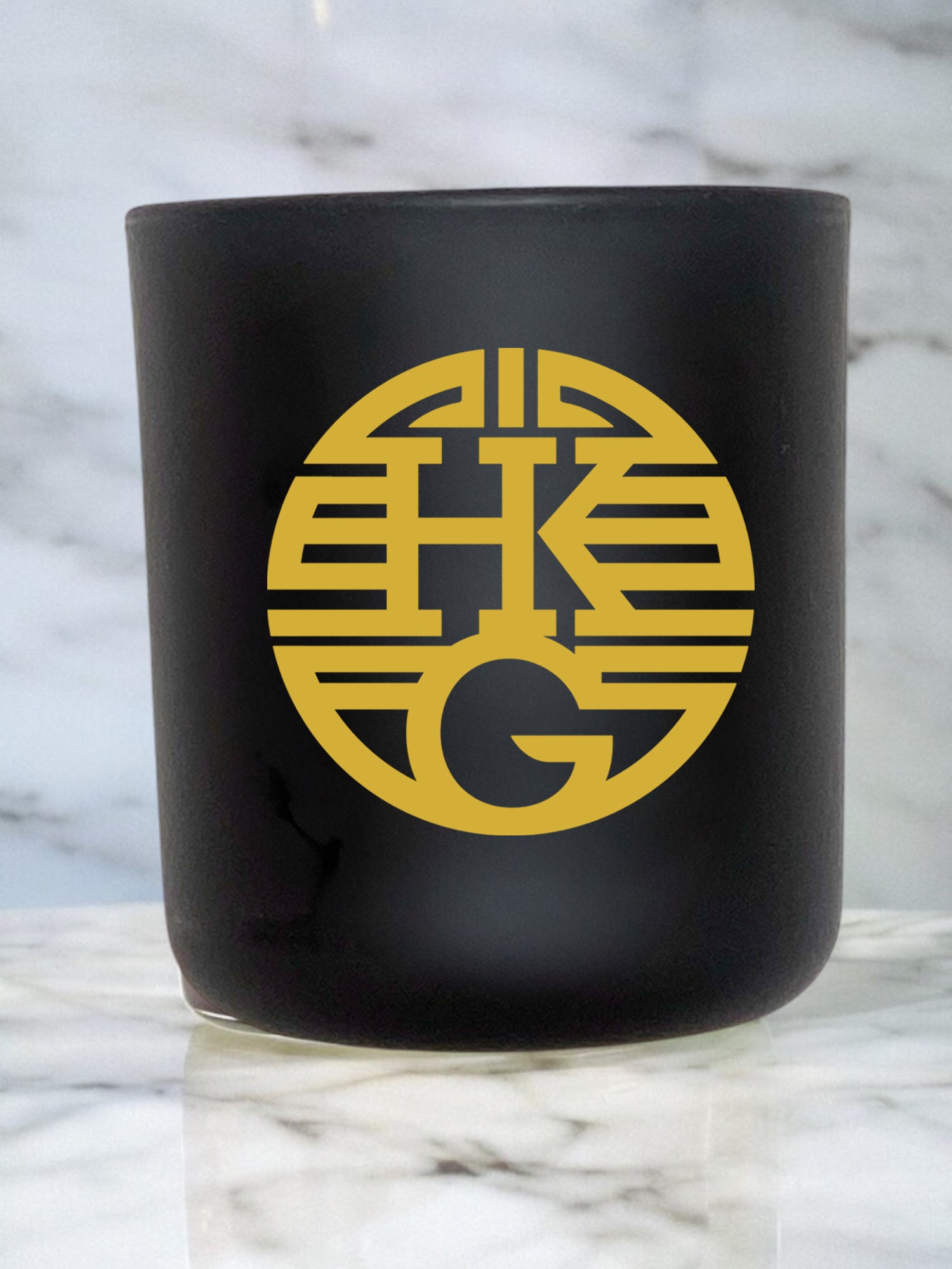 Black candle jar with gold logo on a marble surface