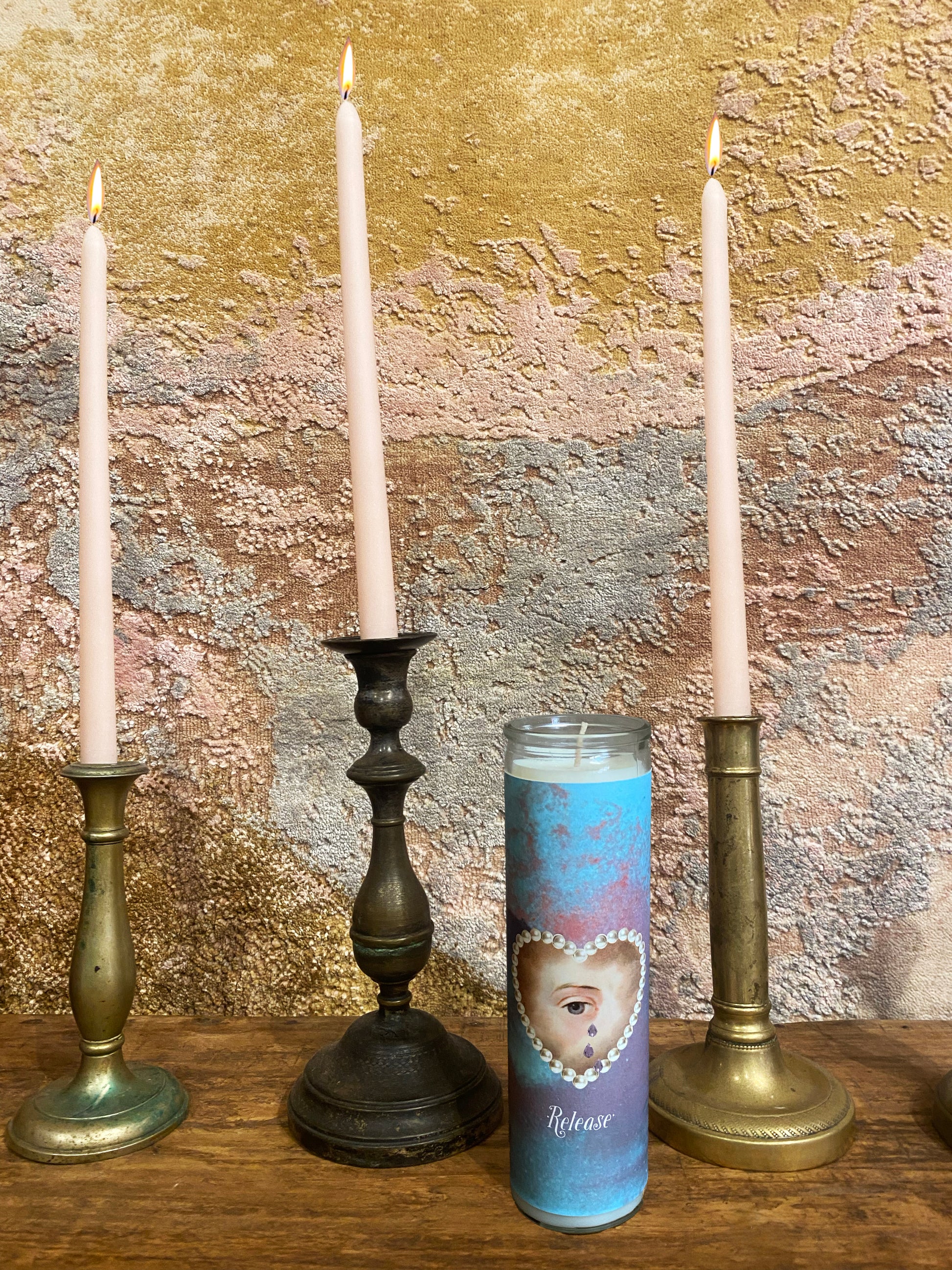 Candle displaying an eye + heart, surrounded by taper candles against a textured background.