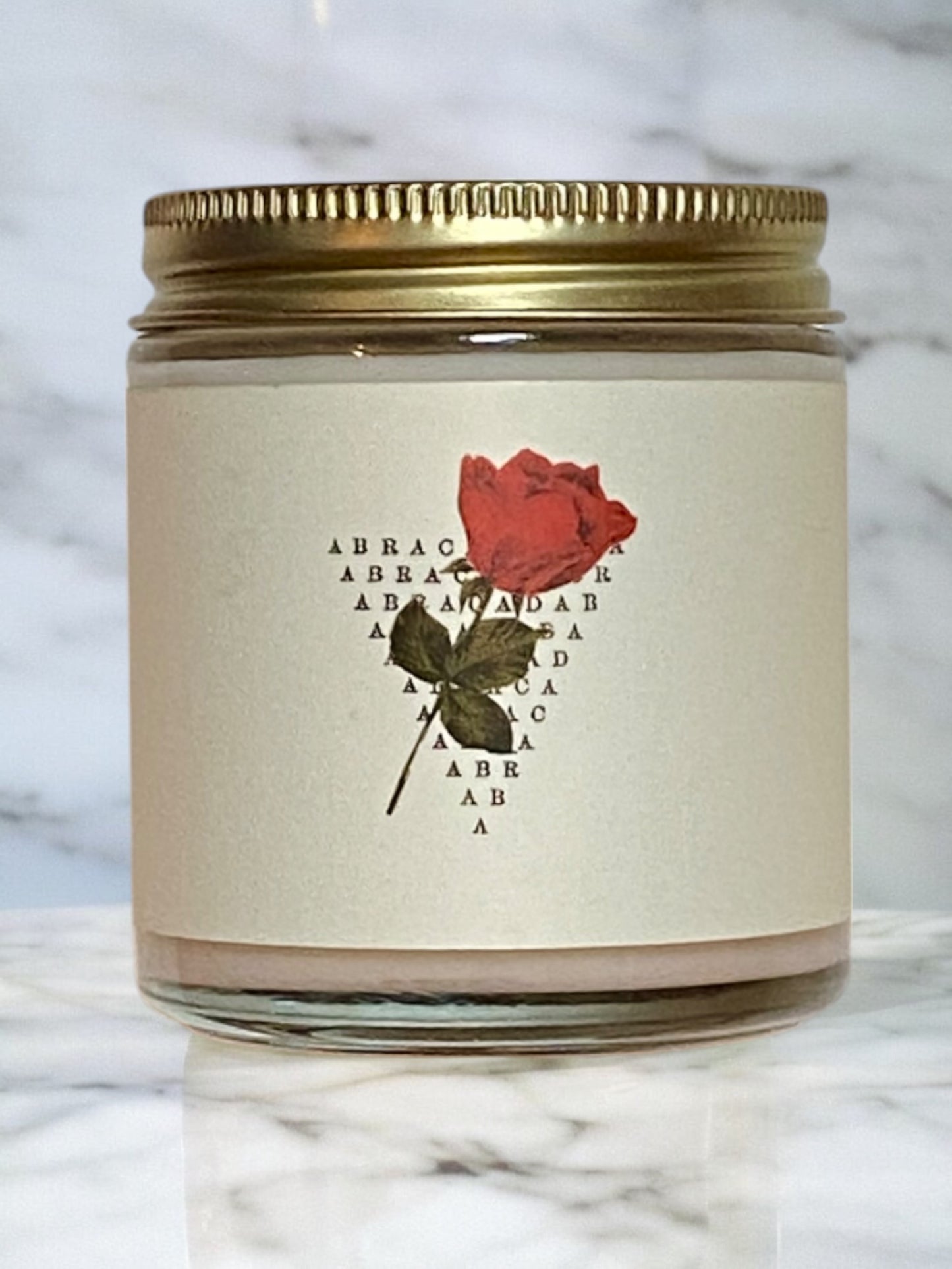 Candle jar with a red rose label on a marble surface