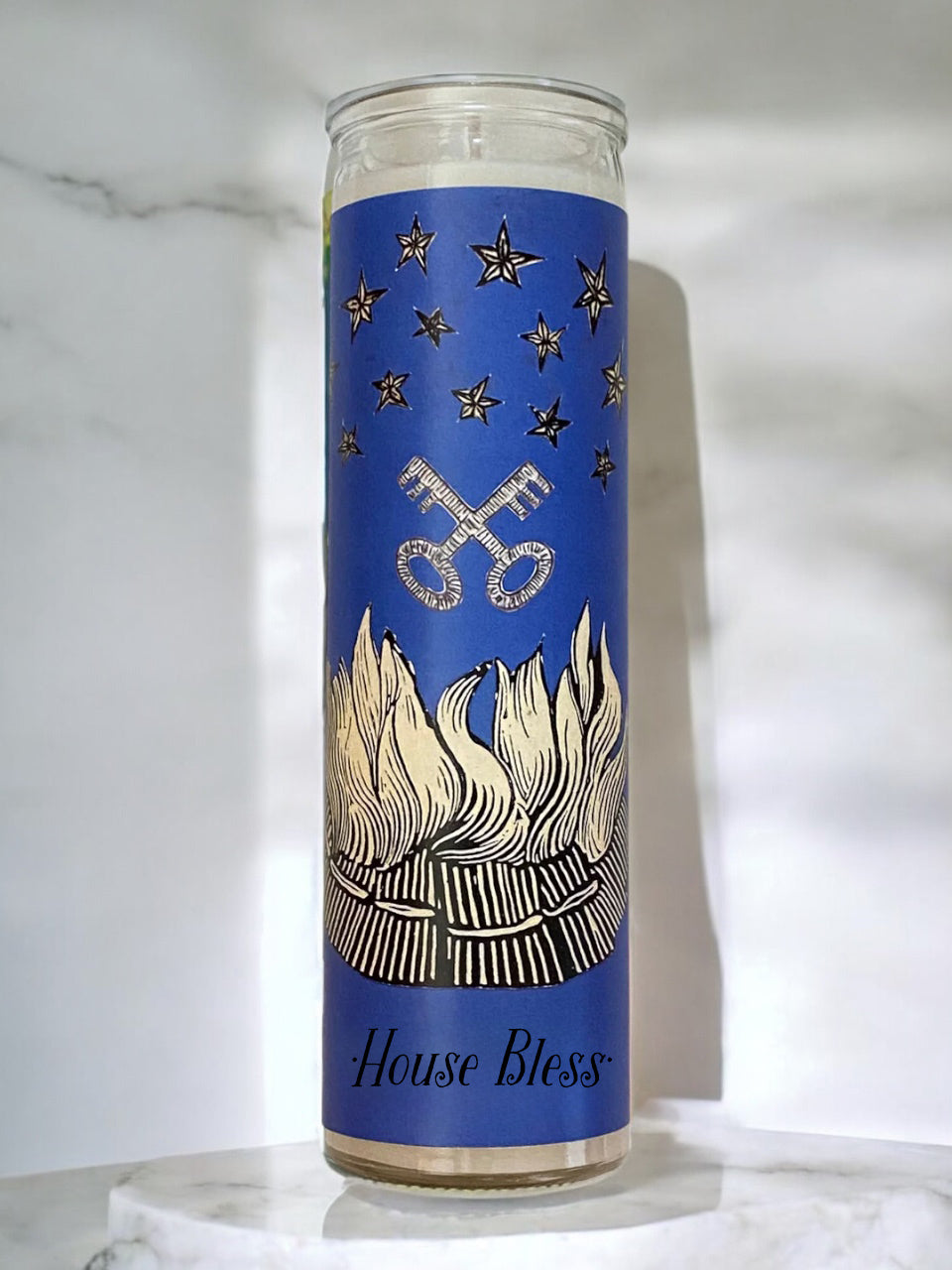 Candle with blue label featuring star and bonfire design and text on a white marble surface.