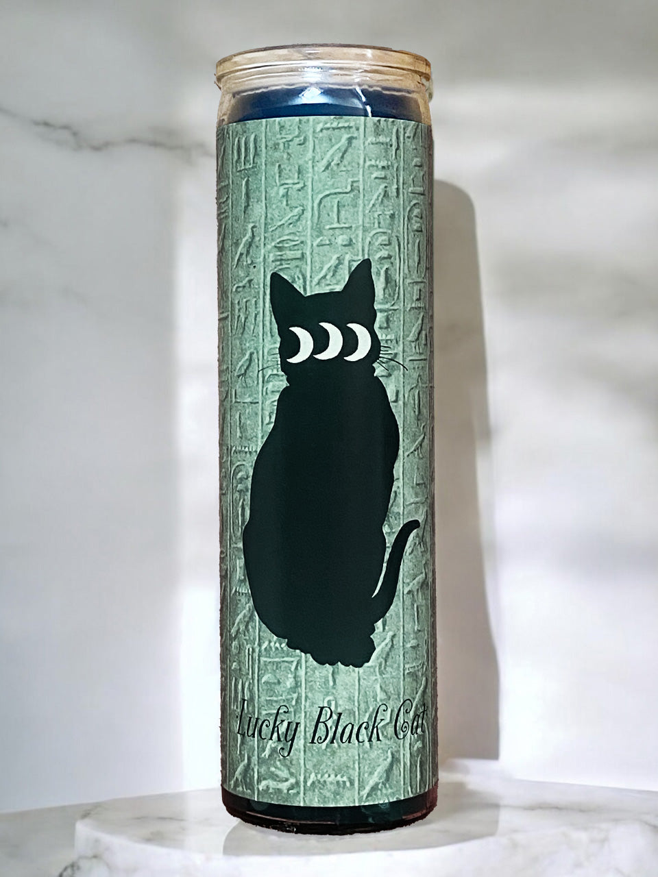 Candle with a black cat silhouette and moon phases design on a textured green background.