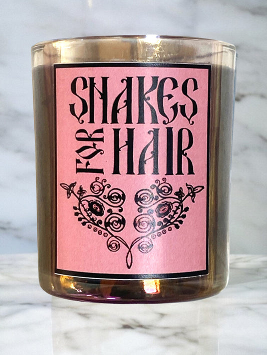 Candle with a pink label reading 'Snakes for Hair' on a marble surface.