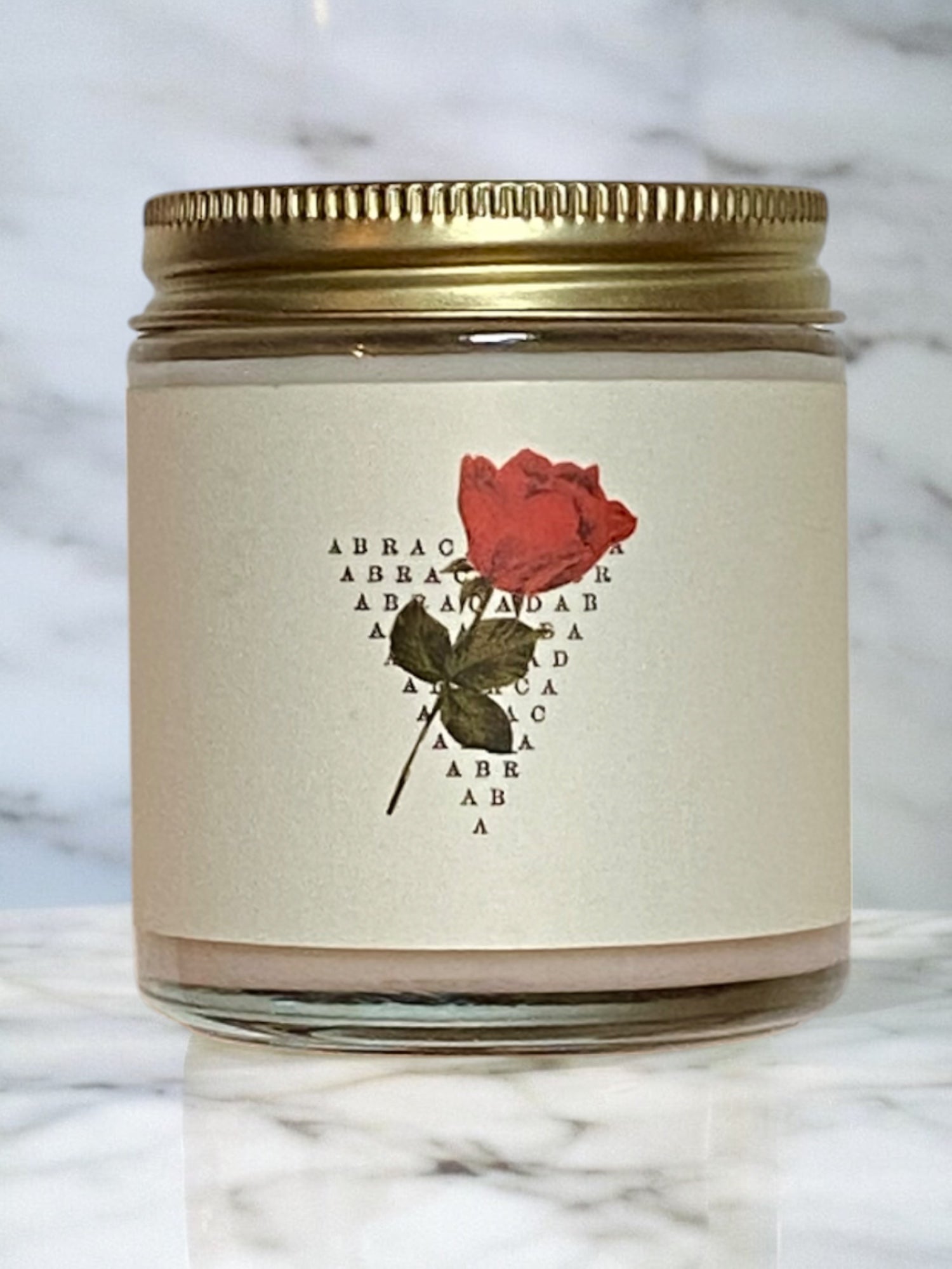 Candle jar with a red rose label on a marble surface